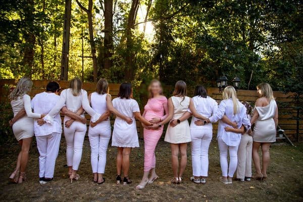 grupa kobiet ubranych na biało, stojących tyłem do kamery, w centrum kadru kobieta w różowej sukience przodem do kamery
